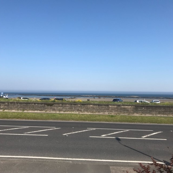 Photo of a car park and the coast in the background with a very blue sky